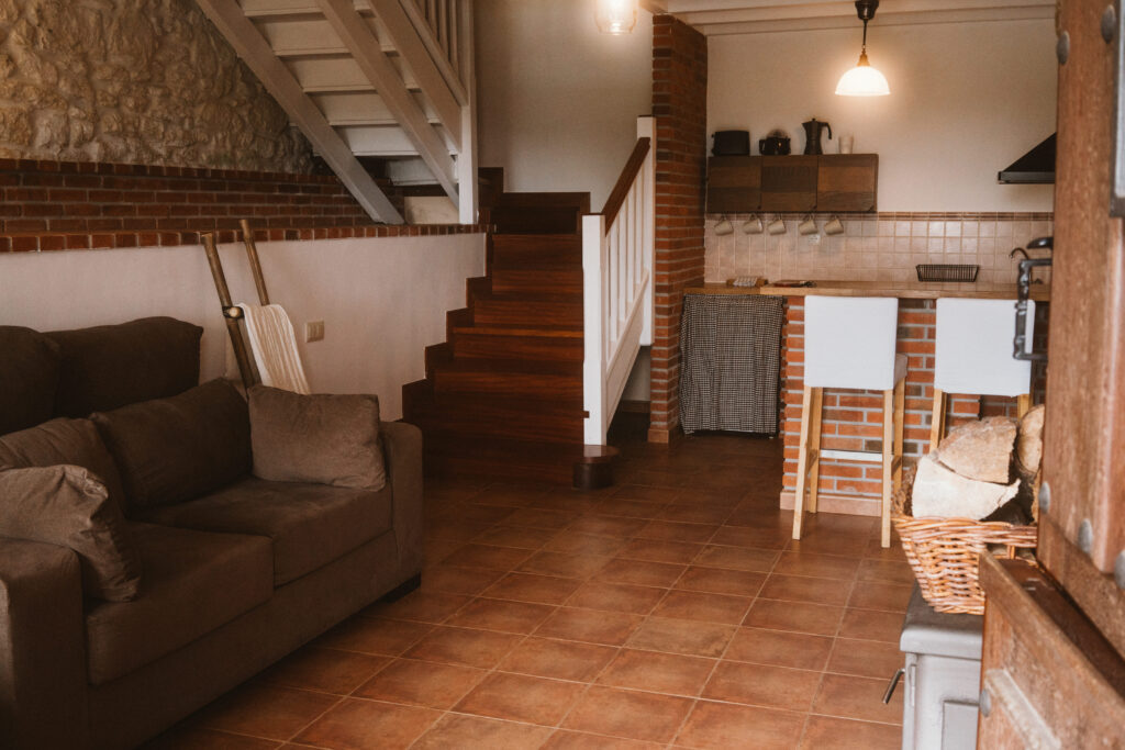 Vista de salón con sofá y cocina en la planta baja de una casa rural de Fuente de Güelo